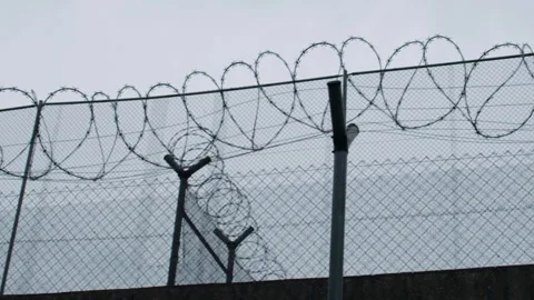 Security fence shows barbed wire at a restricted area under cloudy sky Stock Footage 327872571