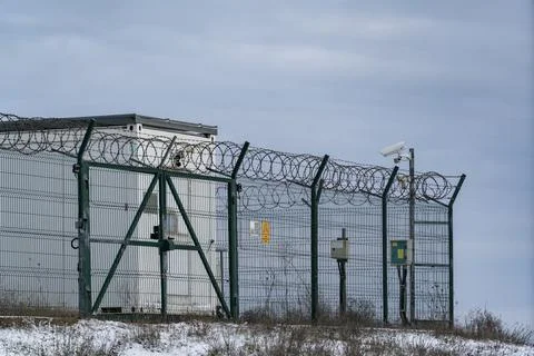 Security fence surrounds facility with watchtower and surveillance camera i.. Stock Photos