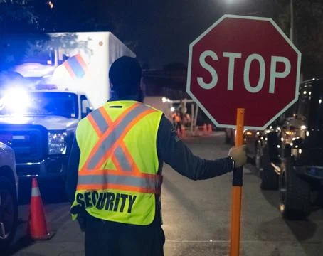 Security guard holding stop/slow down sign at night construction site in Toronto Stock Photos