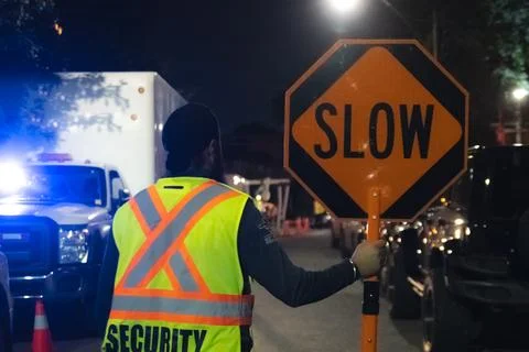 Security guard holding stop/slow down sign at night construction site in Toronto Stock Photos