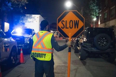Security guard holding stop/slow down sign at night construction site in Toronto Stock Photos