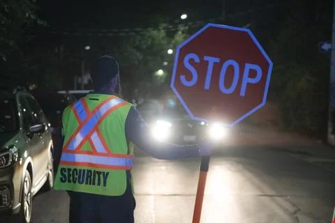 Security guard holding stop/slow down sign at night construction site in Toronto Stock Photos