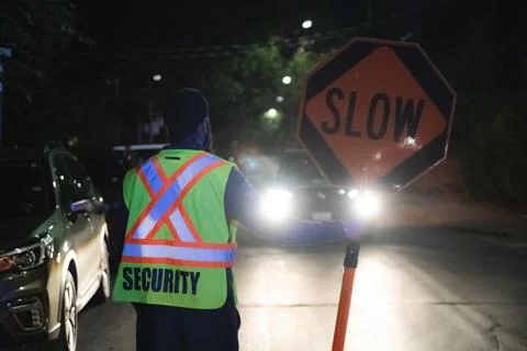 Security guard holding stop/slow down sign at night construction site in Toronto Stock Photos