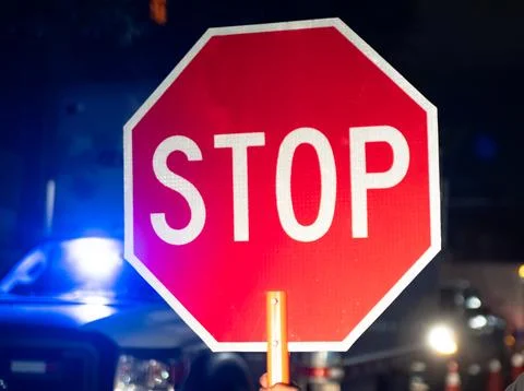Security guard holding stop/slow down sign at night construction site in Toronto Stock Photos