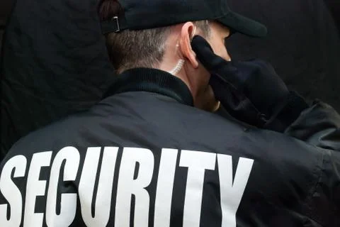 Security guard listens to earpiece, back of jacket showing Stock Photos