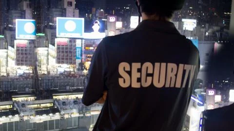 Security guard looking down cityfull of lights at night.. Stockfoto's