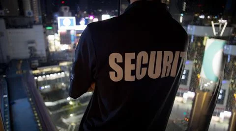 Security guard looking down cityfull of lights at night.. Stock Photos