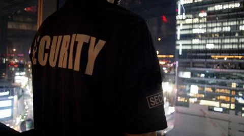 Security guard looking down cityfull of lights at night.. Stock-Fotos