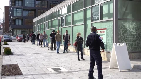 A security guard monitors a socially distanced queue of people waiting outside. Video stock 333427557