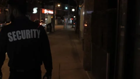 Security guard patrolling streets around commercial building at night Stock Footage 238950122