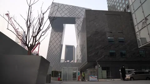 A security guard standing next CCTV headquarters building and cars in Beijing Stock Footage 234313915