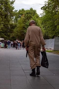 Security guard in tan uniform walking away on city sidewalk with black bag Stock Photos