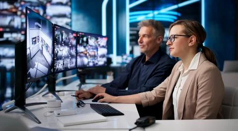 Security Guard Watches Multiple CCTV Screens To Monitor Busy Control Room. Stock Photos