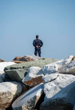 Security man standing alone on big rocks and staring the sea Stock Photos