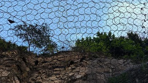 A security mesh net covering a rocky slope. Stock Photos