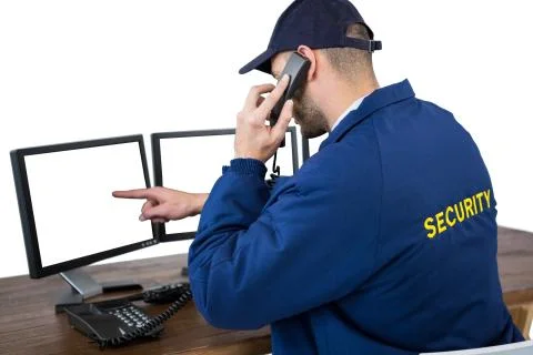 Security officer talking on phone while pointing at computer monitors Stock Photos