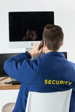 Security officer talking on telephone while looking at computer monitors Stock Photos