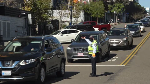 Security person waves on long line of cars entering vaccination super station Stock Footage 147367336
