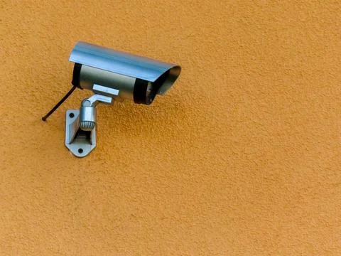 Security surveillance camera mounted on textured yellow wall Stock-Fotos