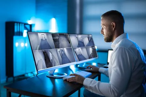 Security System Operator Looking At CCTV Footage At Desk Foto stock