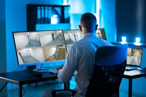 Security System Operator Looking At CCTV Footage At Desk Foto stock