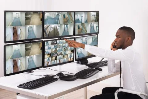 Security System Operator Talking On Phone While Looking At CCTV Footage Foto stock