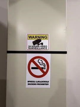 Security warning and no smoking signs mounted on neutral wall with vertical.. Stock Photos