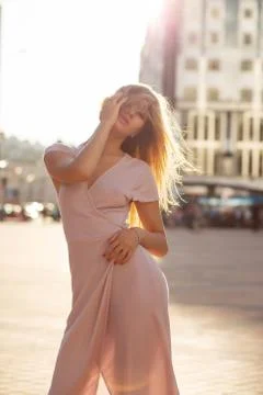 Seductive blonde model in trendy pink dress posing at the street in soft even Stock Photos
