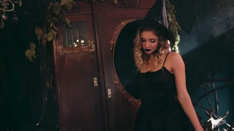 Seductive blonde witch wearing a black dress and hat dancing mysteriously in a 스톡 동영상 330786810