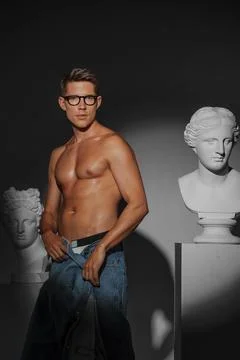 Seductive male model poses in a studio next to classical Greek bust sculpture Stock Photos