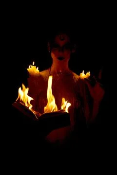 Seductive witch with burning book on black background Foto stock