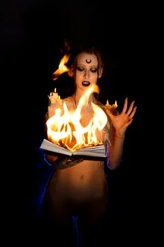 Seductive witch with burning book on black background Foto stock