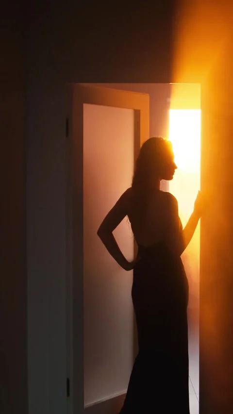 Seductive young beautiful woman opens door with sun light rays, black silhouette Stock Footage 332209687