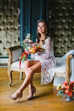 Seductive young bride posing with gorgeous bridal bouquet on a sofa Stock Photos