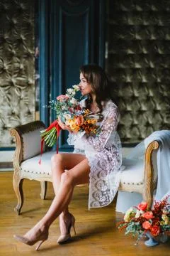 Seductive young bride posing with gorgeous bridal bouquet on a sofa Stock Photos