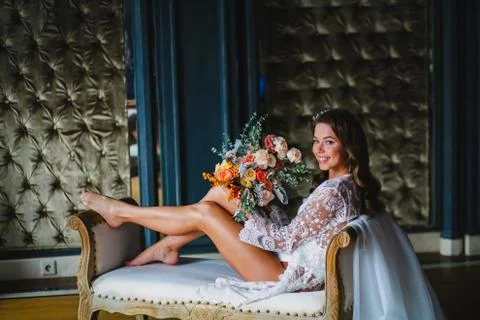 Seductive young bride posing with gorgeous bridal bouquet on a sofa Stock Photos
