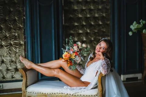 Seductive young bride posing with gorgeous bridal bouquet on a sofa Stock Photos