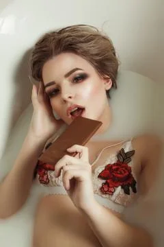 Seductive young model with evening makeup takes a bath with milk and eats cho Foto stock