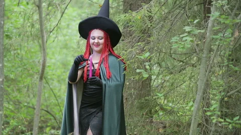 Seductive young witch with red hair and a pointed hat and a black cloak conjures 库存影片 119925264