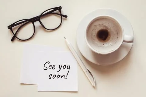 See you soon note, empty cup with coffee leftovers, eyeglasses and pen on whi Fotos Stock