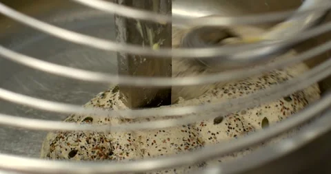 Seeded bread dough folding around central mixer blade in stainless bowl, with Stock Footage 344597640