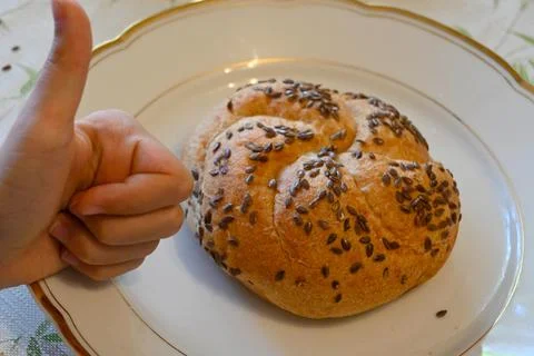 Seeded Kaiser roll on a decorative plate with thumbs-up gesture Foto stock