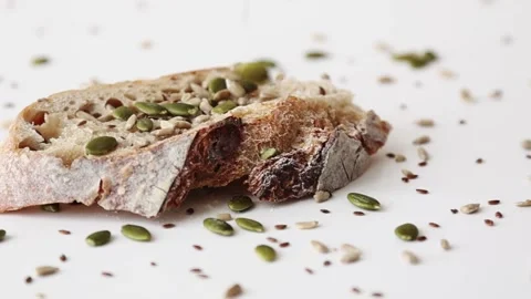 Seeds falling on piece of fresh baked sourdough bread on white surface Stock Footage 196003606