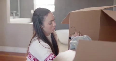 Seeing partial mark, Asian woman kneeling by tub packing linens, labeling box Stock Footage 345588293