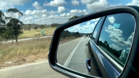 Seeing white clouds and blue sky from a rear mirror while driving on a highway Stock Footage 167944566