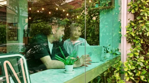 Seen through a cafe window, small business partners collaborate on a laptop. Stock Footage 310296735