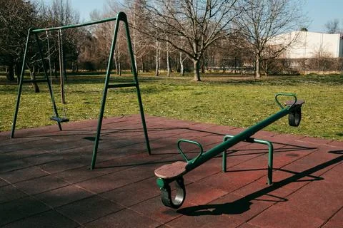 Seesaw and swing set in an empty playground on rubber safety flooring. Outdoo Stock Photos