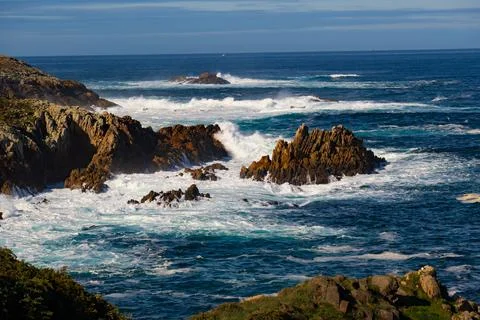 Seething long ocean waves with white foam crashing against coastal rocks (sea Stock Photos