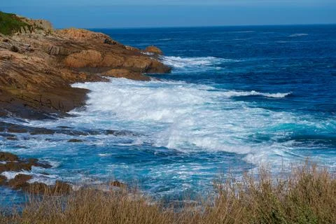 Seething long ocean waves with white foam crashing against coastal rocks (sea Stock Photos