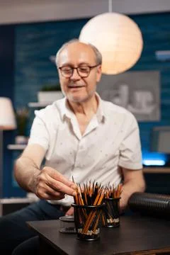 Selctive focus on elderly man illustrator selecting sharp hb pencil to create Stock Photos